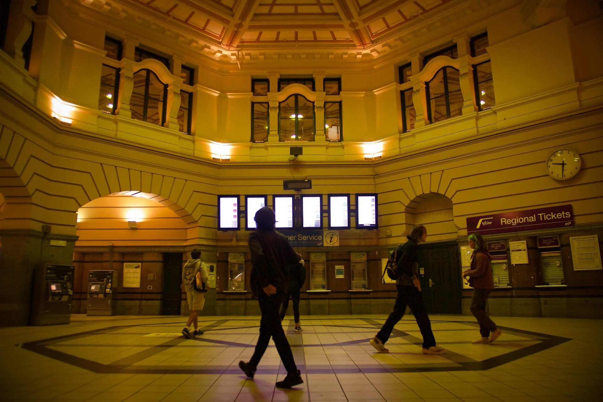 People walk through the entrance hall at Flinders Street Station in Melbourne at night.