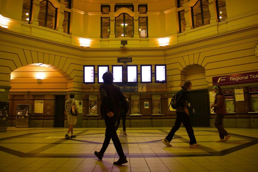 People walk through the entrance hall at Flinders Street Station in Melbourne at night.