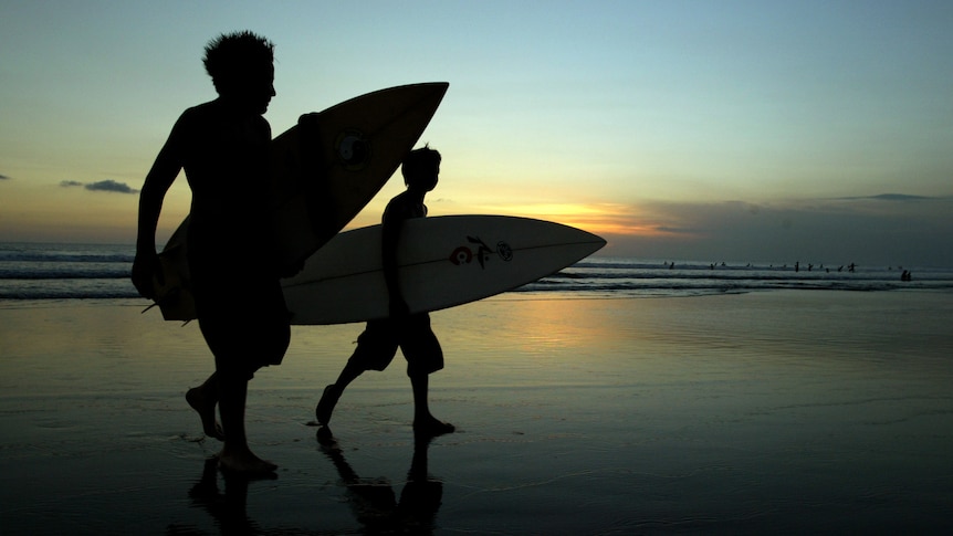 Two young surfers walk in from the surf at sunset on Legian beach near Kuta on Bali.