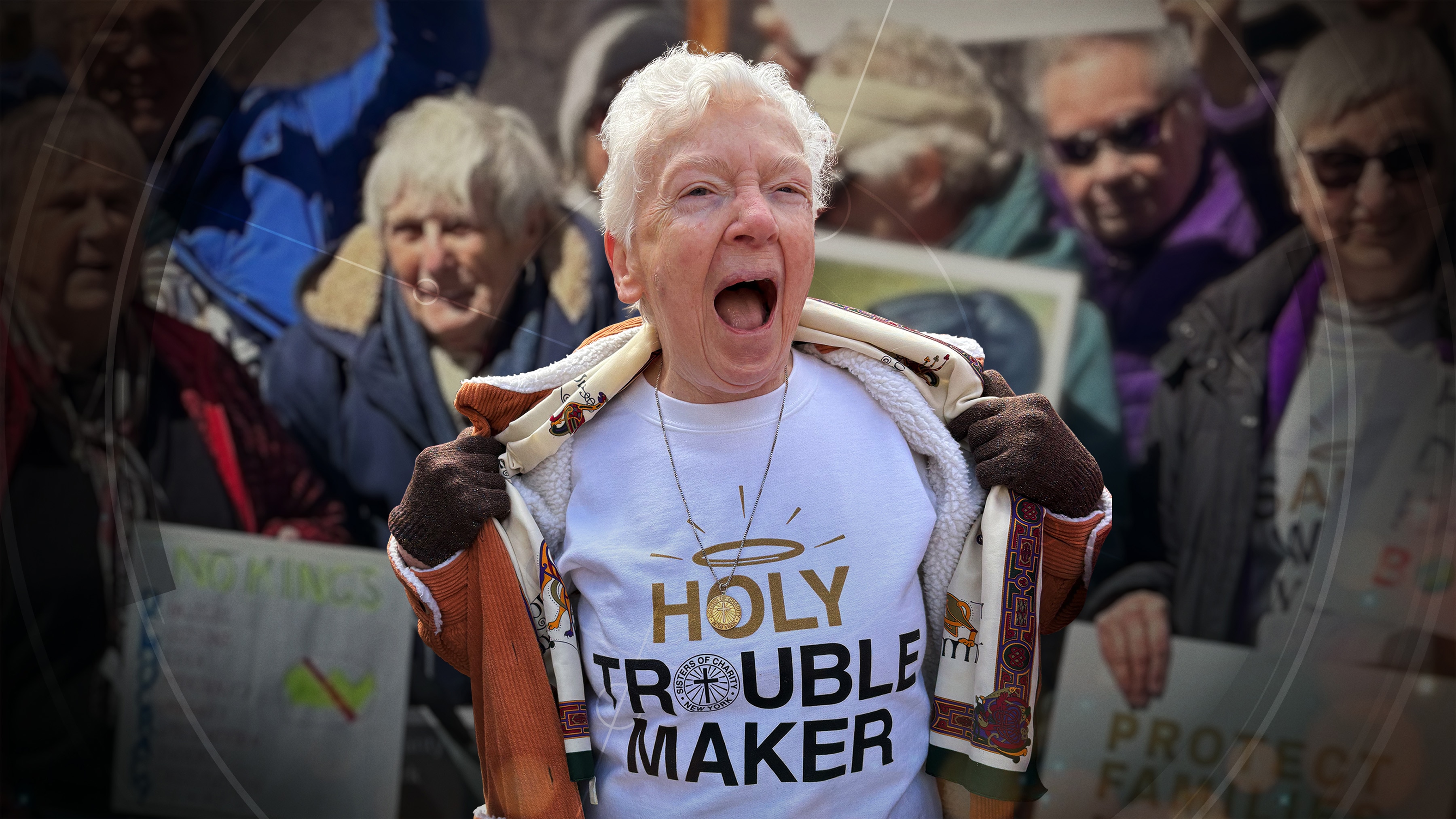 Woman with short grey hair in a crowd of protestors screams and opens jacket to show T shirt saying Holy Trouble Maker