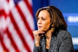 Kamala Harris in front of a row of US flags resting her head on her chin