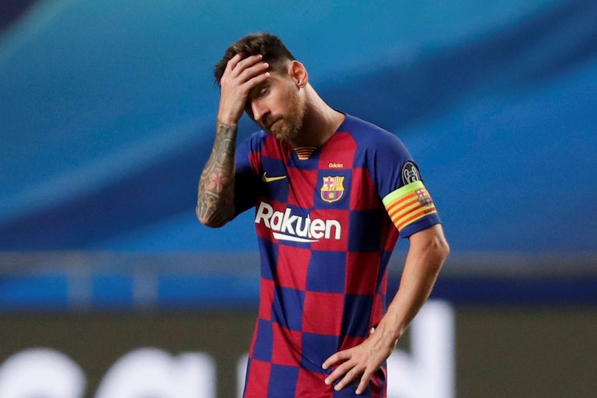 Lionel Messi holds his hand to his forehead as he stands on his own.
