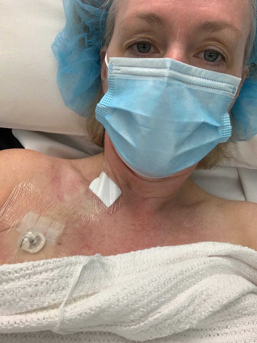 Jo Woods lies in a hospital gown, with a mask and a port in her chest.