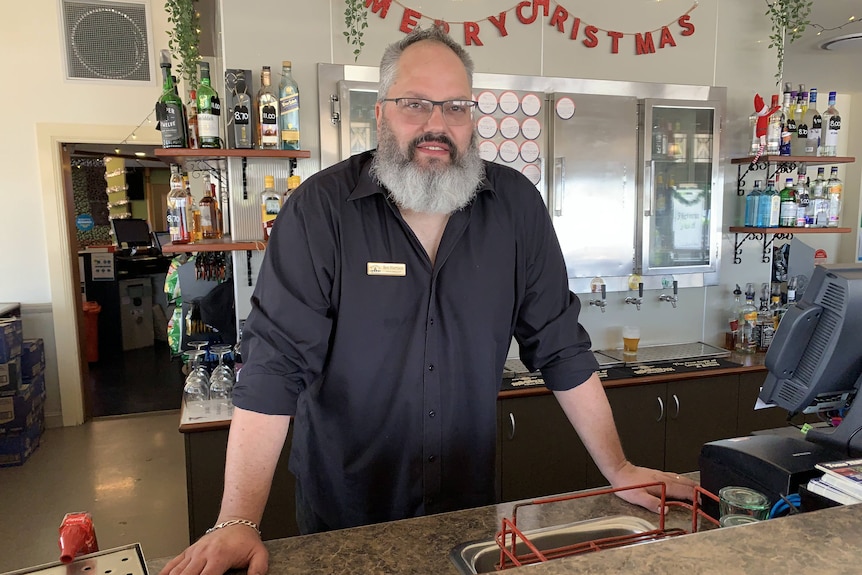 A bearded man stands behind a bar.