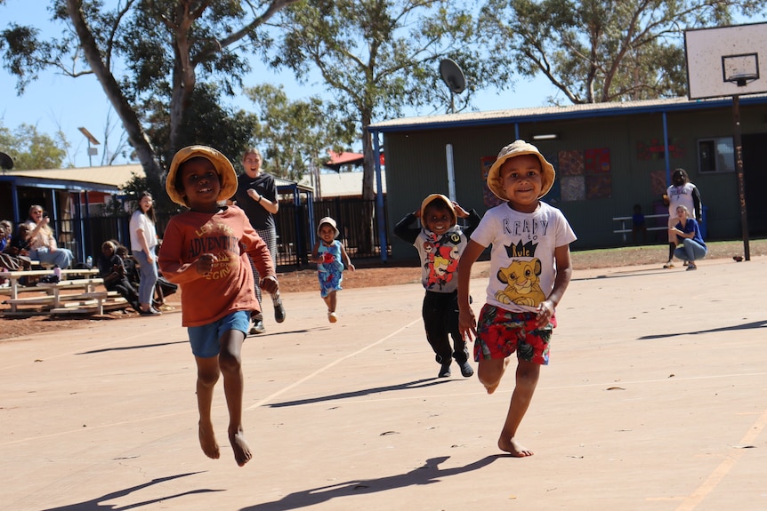 very young Aboriginal children running towards the camera, smiling, as they race across a concrete sports ground