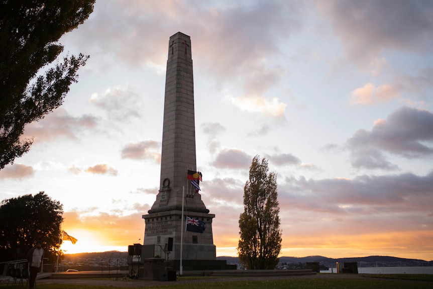 A long column structure surrounded by flags as the sun rises.