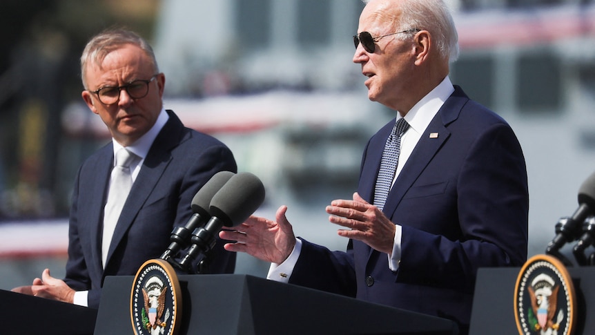 Anthony Albanese (left) stands and shakes hands with Joe Biden in front of US and Australian flags.