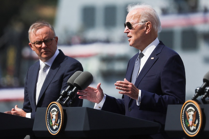 Anthony Albanese (left) stands and shakes hands with Joe Biden in front of US and Australian flags.