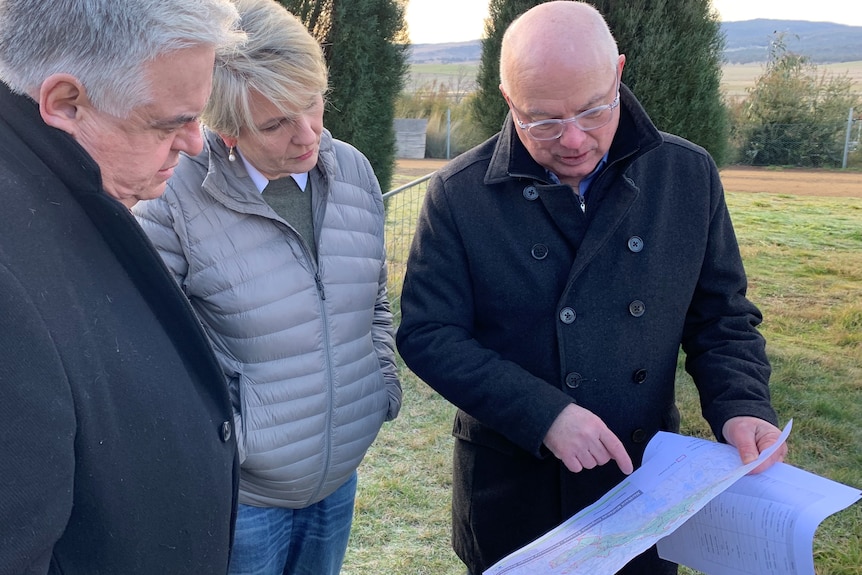 Three people looking at irrigation plans while standing in a paddock in Tasmania.