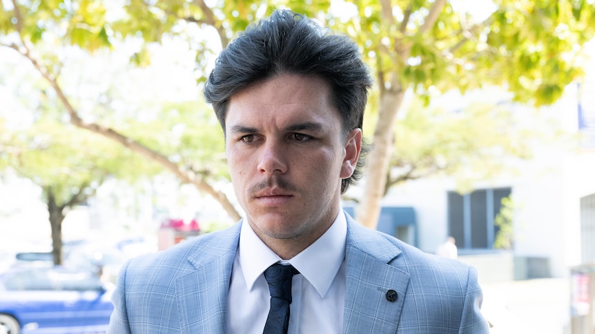 AN AFL footballer in a suit and tie is pictured on his way to a courthouse for a court appearance.
