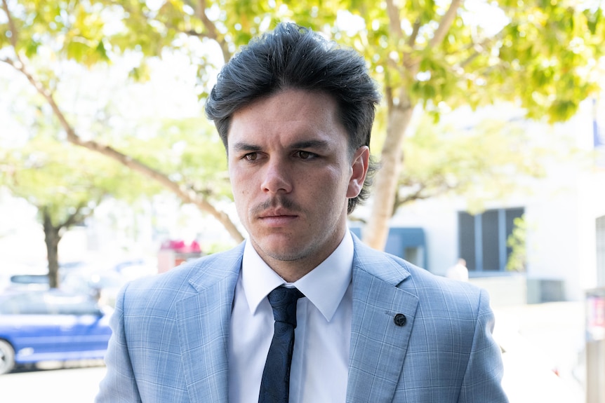 AN AFL footballer in a suit and tie is pictured on his way to a courthouse for a court appearance.