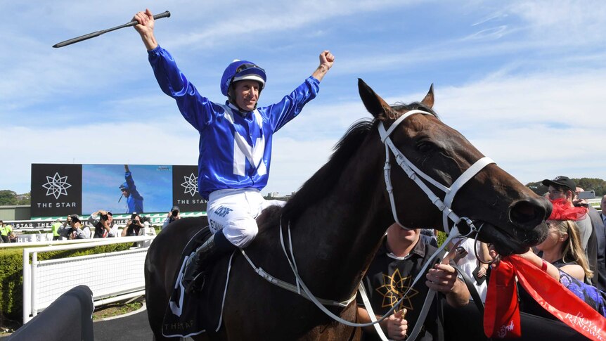 Hugh Bowman spreads out his arms in celebration while on top of Winx.