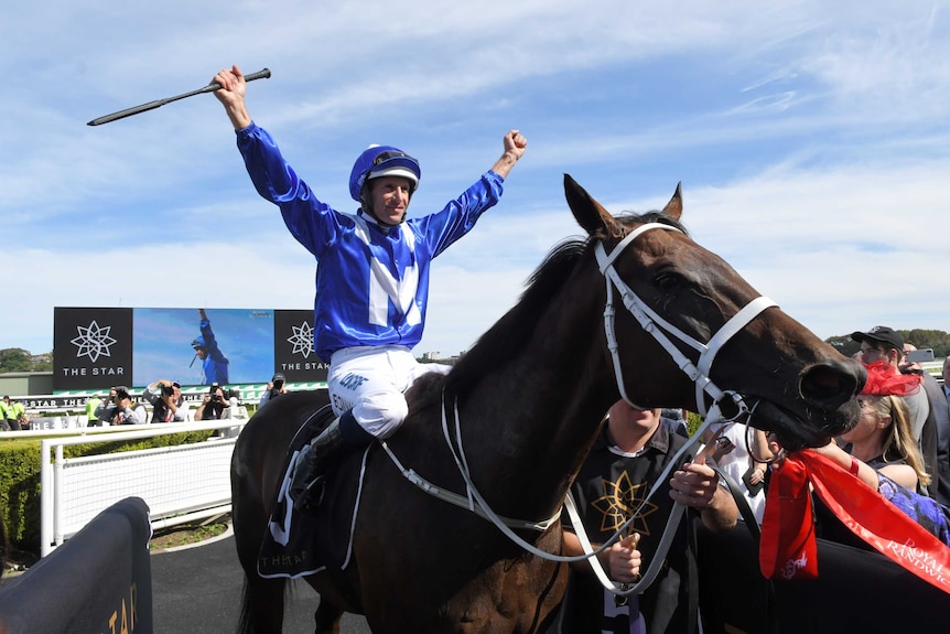 Hugh Bowman spreads out his arms in celebration while on top of Winx.