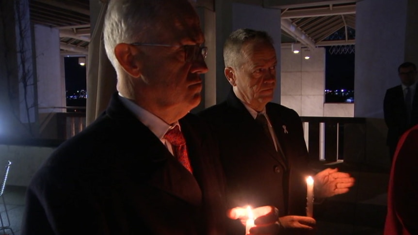 Malcolm Turnbull and Bill Shorten stand together in the dark at Parliament House in Canberra holding candles.