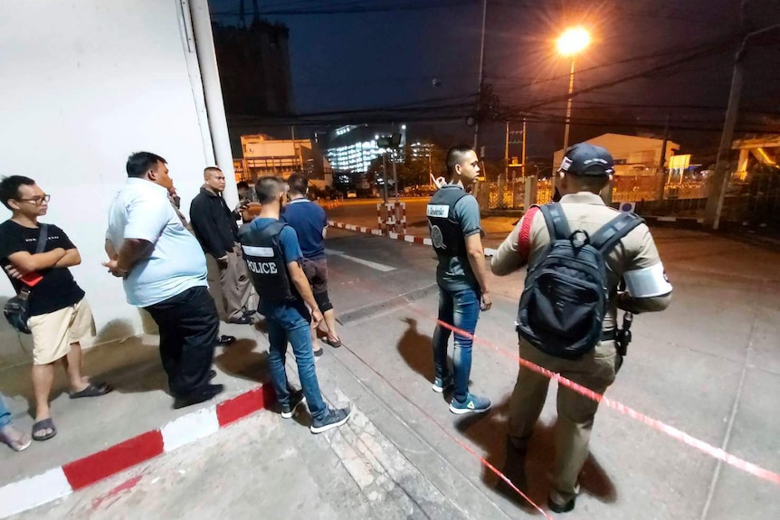 Police stand on a street at night.