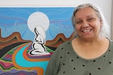 Woman smiling on right in front of indigenous dot painting of swirls and pregnant woman