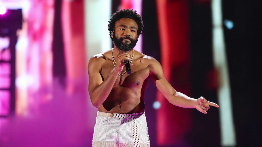 A shirtless Childish Gambino performs on stage.