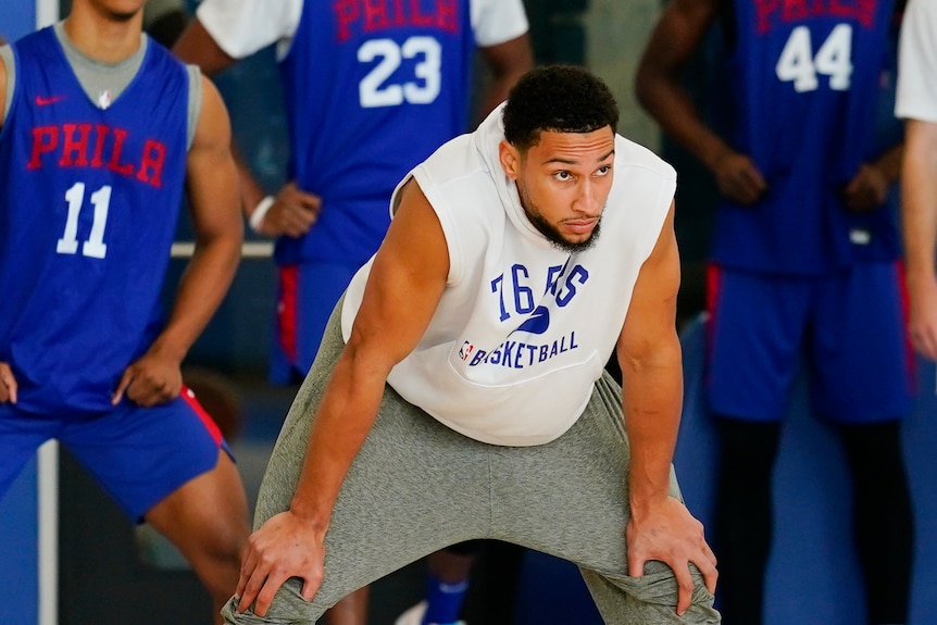 Basketball player in singlet and track pants with his hands on his knees.