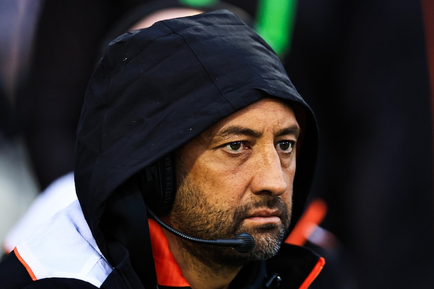 Benji Marshall, wearing a hoodie and a head set, watches a game from the sideline