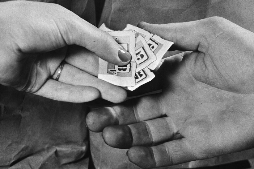 A black and white scanned image shows a close-up of hands exchanging small paper tickets.