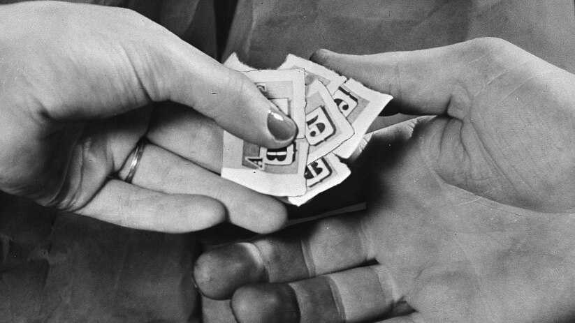 A black and white scanned image shows a close-up of hands exchanging small paper tickets.