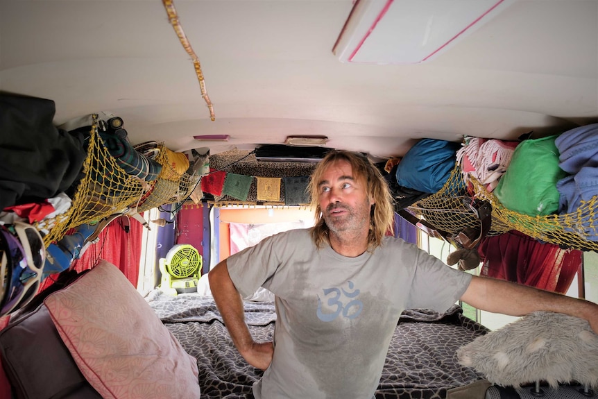 Man standing in a campervan-style converted bus looking to the top left of frame.