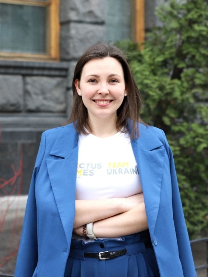 Woman wearing a blue blazer over an Invictus T-shirt, smiling.