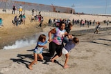A mother grasps her two children by the hand as the trio sprints from a tear gas cannister along US-Mexico border