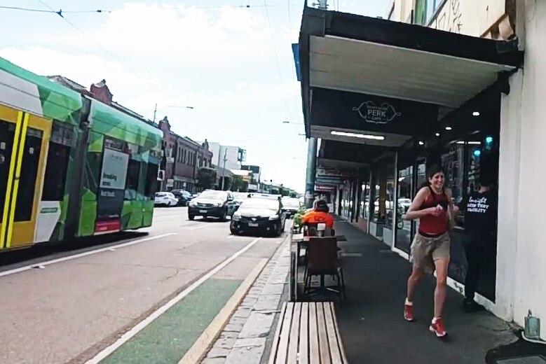 A woman jogs down a footpath, with a tram on the road next to her.
