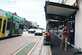 A woman jogs down a footpath, with a tram on the road next to her.
