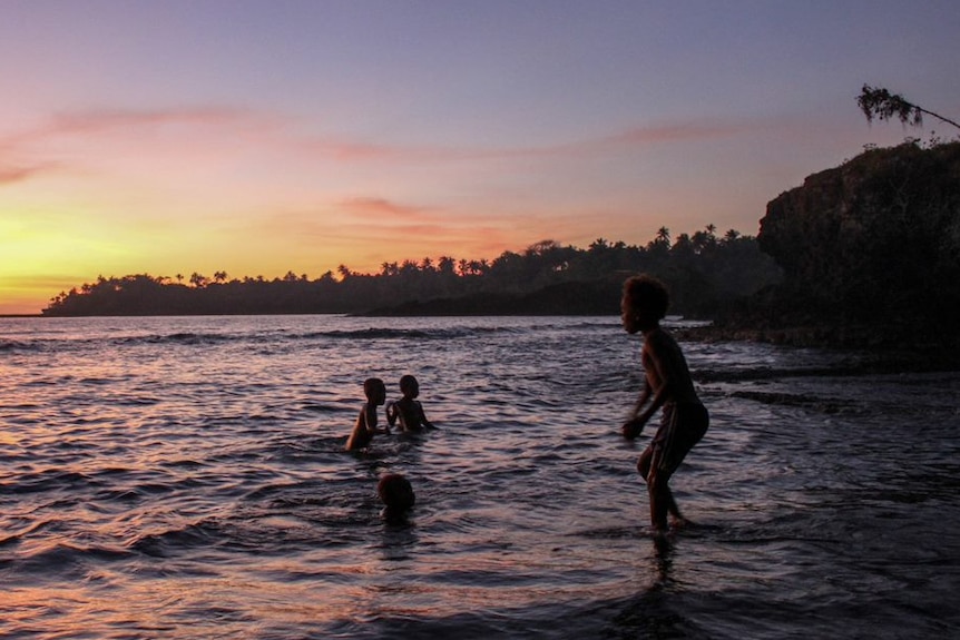 Children in Vanuatu play in the beach at sunset.