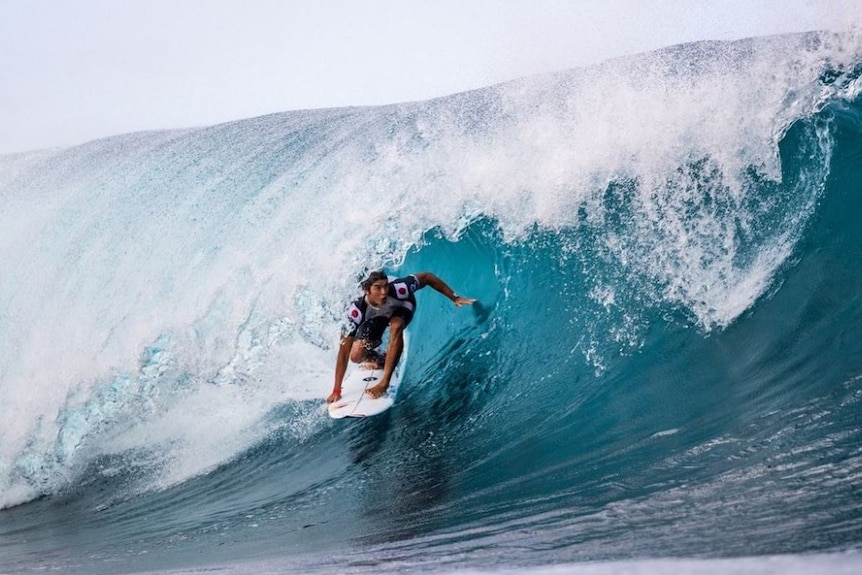 Kanoa Igarashi crouches down on his board as he rides a wave that breaks over his head
