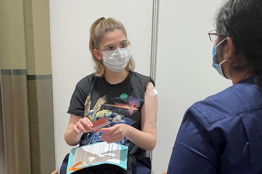 A young woman wearing a face mask speaks to a health professional.