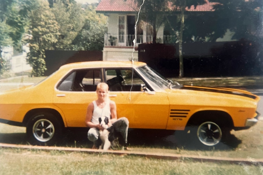 a yellow holden monaro with a teenage boy with his dog squatting down in front of it.