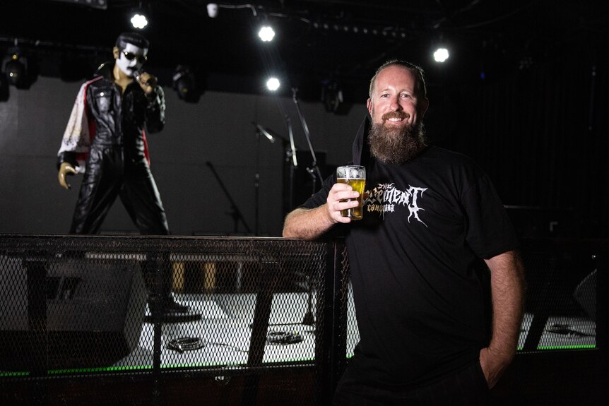 A man in a black shirt holds a beer in one hand.