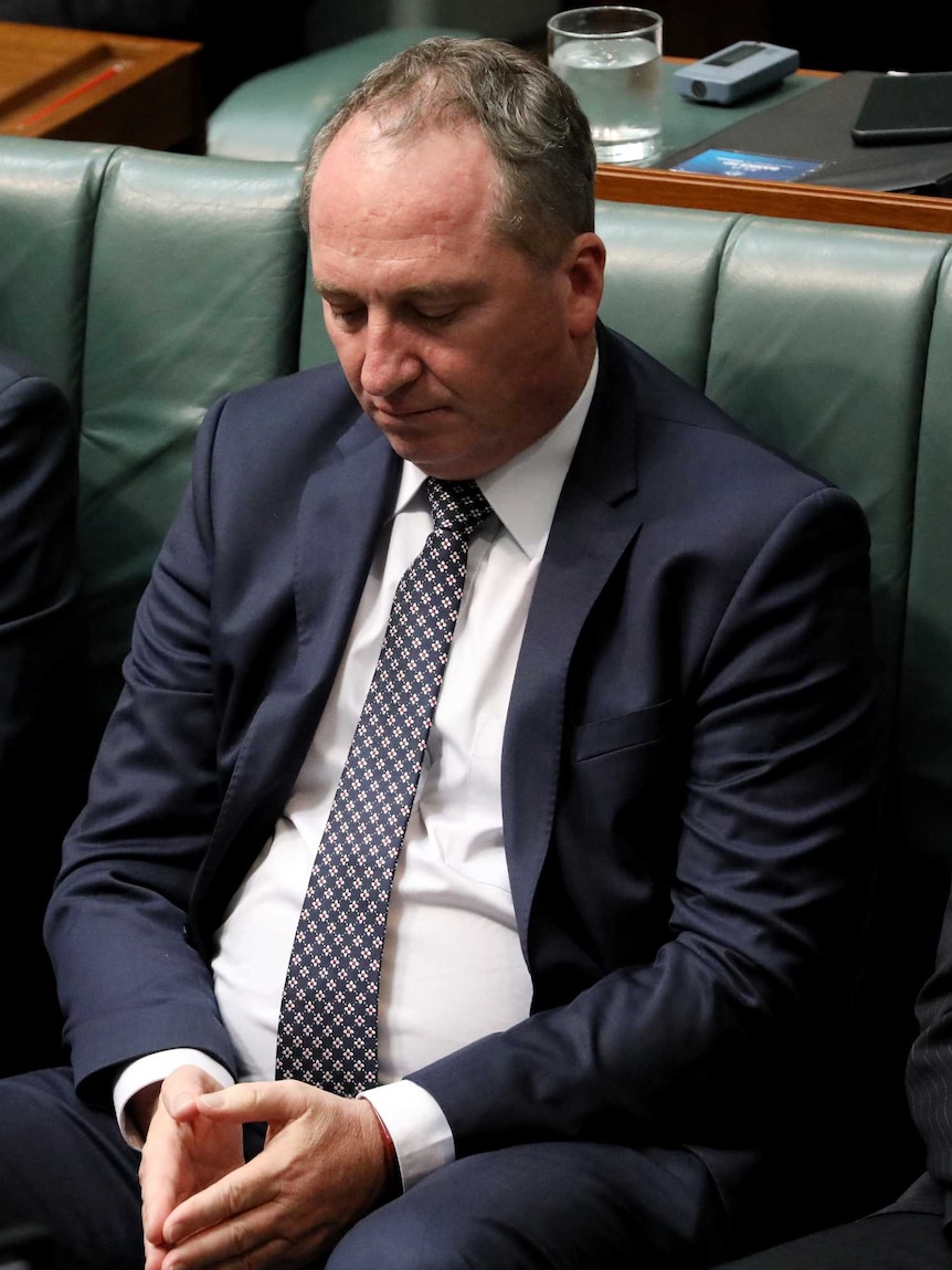 Barnaby Joyce gazes down towards his hands, which are clasped in his lap. Next to him are Christopher Pyne and Ken Wyatt