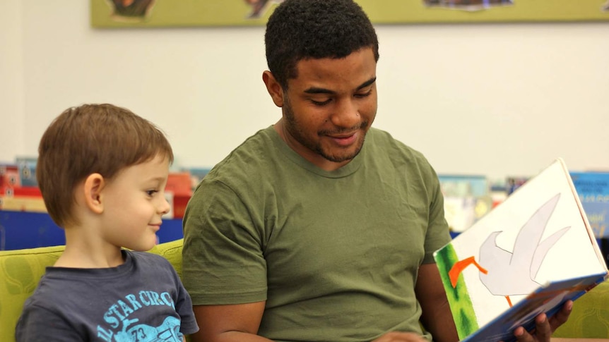 A man and male child sit on a couch reading a book together