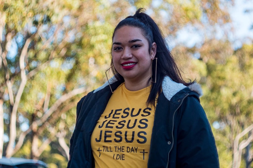 Ana Makahununiu, a Tongan woman, smiling. She is wearing a t-shirt that says 'Jesus Jesus Jesus till the day I die.'