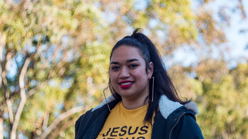 Ana Makahununiu, a Tongan woman, smiling. She is wearing a t-shirt that says 'Jesus Jesus Jesus till the day I die.'