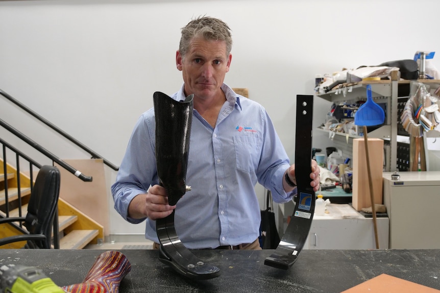 A man in a blue shirt holds two prosthetic legs in his hands