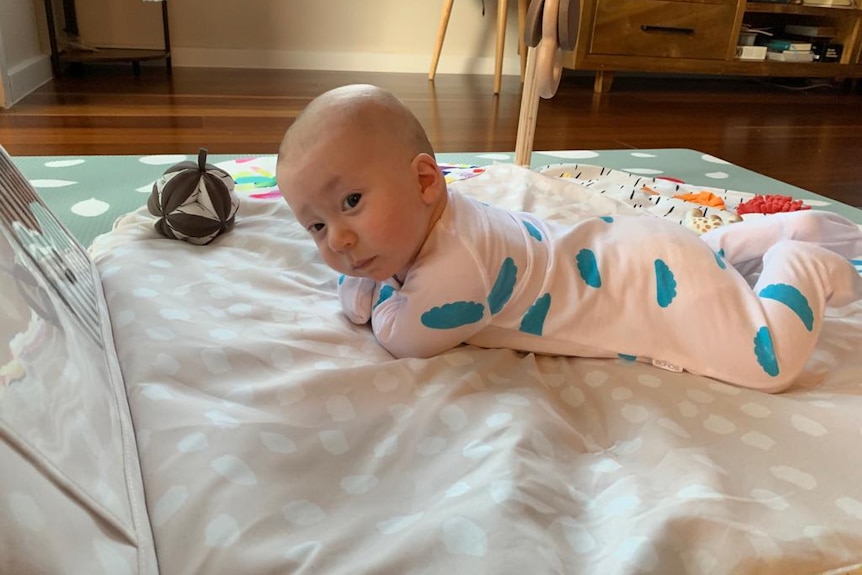 Baby Menasheh in a onesie laying on his tummy