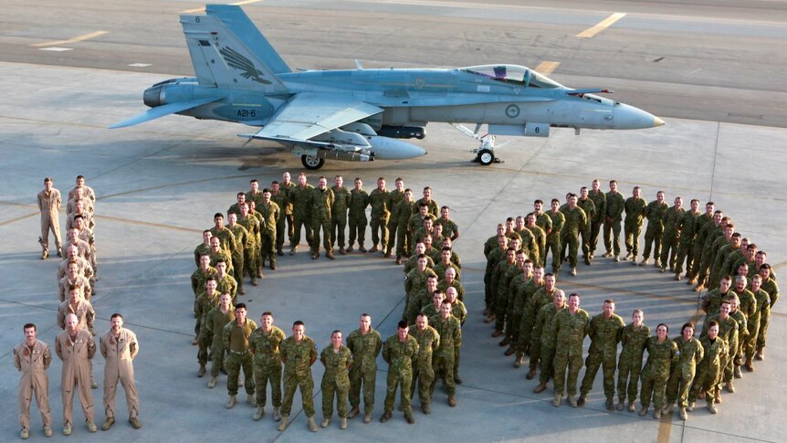 RAAF personnel form a human '100' on the tarmac alongside a fighter jet.