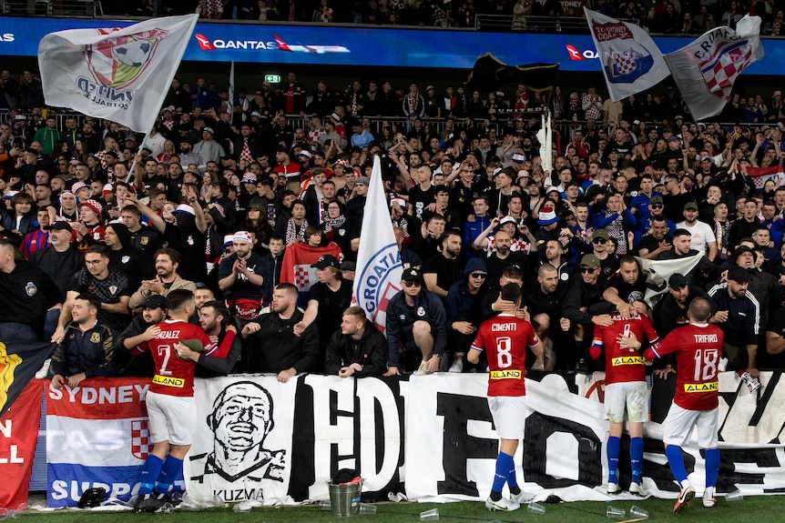 Supporters of a soccer team wearing red, white and blue wave flags and hold banners after a game