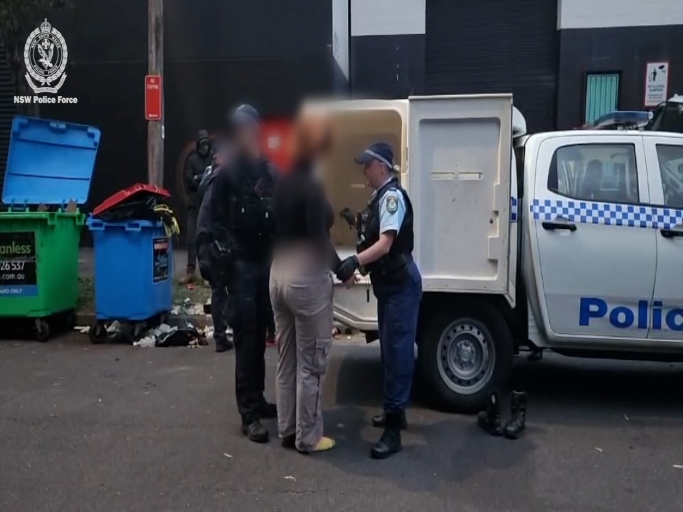 A woman, with her face blurred, being led into the back of a police car.