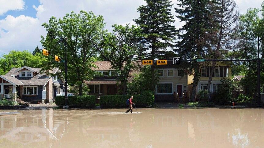 A woman walks down a flooded street in the Elbow Park area of Calgary