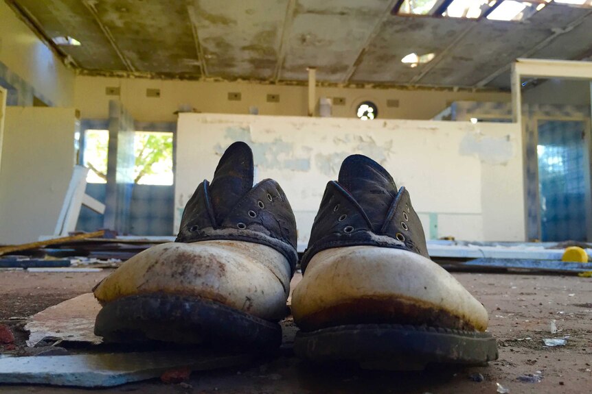 A close-up of a pair of tattered golf shoes in a dilapidated building