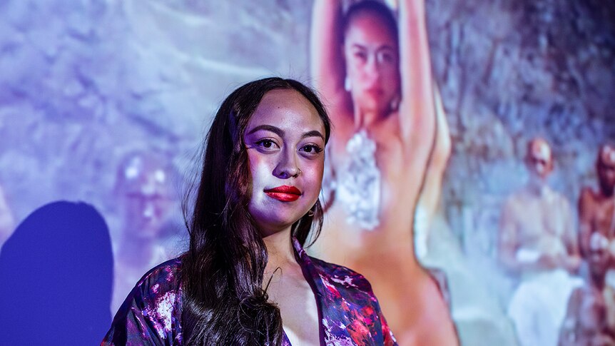 Colour photo of artist Caroline Garcia standing in front of video wall projection.