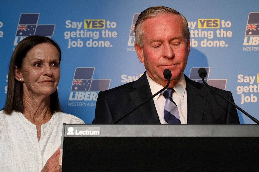 Colin Barnett appears forlorn standing at a pedestal on a stage alongside his wife Lyn.