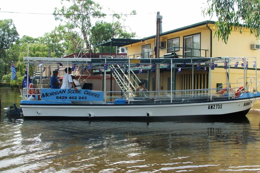 Un bateau de tourisme 'Morgan Scenic Cruises' est à côté d'une cabane jaune inondée.
