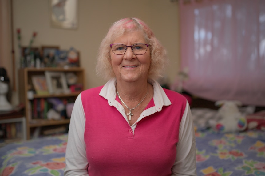 Dianne smiles, wearing a pink top and pink glasses.